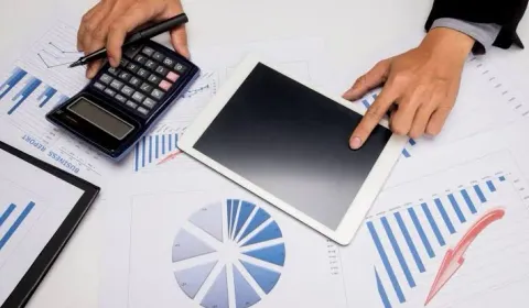 Masa üzerinde hesap makinesi, tablet ve mali evraklarla SGK işlemleri çalışması